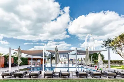 a pool with chairs and umbrellas in front of a building at Beachy Getaway in JBR with Private Beach Access in Dubai