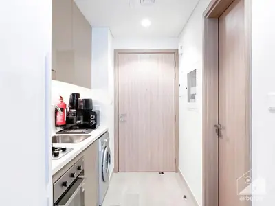 a kitchen with a door leading into a kitchen with white cabinets at Urban Charm Studio with Balcony in Riviera in Dubai