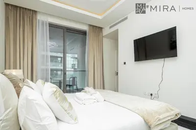 a bedroom with a white bed with a flat screen tv at Mira Holiday Homes - Lovely new 1 bedroom in Downtown in Dubai