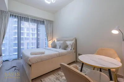 a bedroom with a bed and a table and a window at Savis Homes - Azizi Riviera 43 - Chic Studio Near Downtown and Business Bay in Dubai