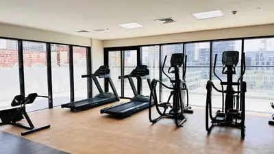 a gym with several tread machines in a room with windows at Modern 1-Bedroom La Perla Apartment JVC with Infinity Pool & Kids’ Zone in Dubai