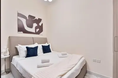 a white bedroom with a large bed with blue pillows at Serene Studio APT with Pool and Gym in Dubai
