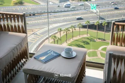 a cup of coffee and a book on a chair in front of a window at Manzil - 1BR Apartment in Farhad Aziz Residence with Burj View in Dubai