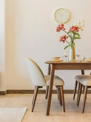 a dining room table with a vase of flowers and a clock at Elegant One Bed Apartment - Hameni Tower,JVC in Dubai