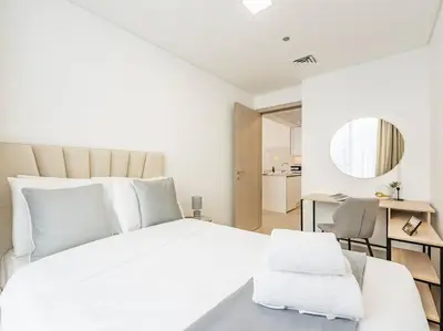 a white bedroom with a large white bed and a desk at Modern Spacious- 2 BR with Pool & Gym- Luma 22 JVC in Dubai