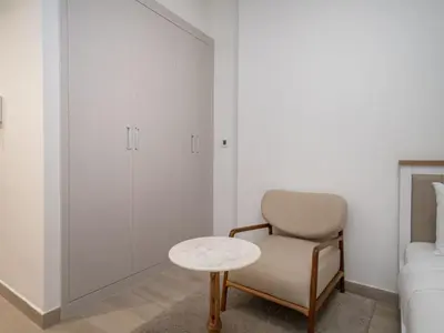 a white bedroom with a chair and a table at Bright JVC Studio - Serenity Escape in Dubai