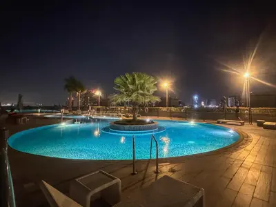 a swimming pool at night with a palm tree in it at Bright JVC Studio - Serenity Escape in Dubai