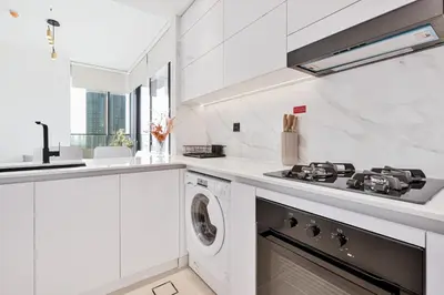 a white kitchen with a stove and a washing machine at Savis Home - Enjoy the City Skyline View 1BR in Binghatti Venus JVC in Dubai