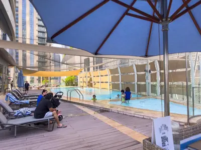 a woman sitting on a bench next to a swimming pool at 1BHK in Damac Masion mall street in Dubai
