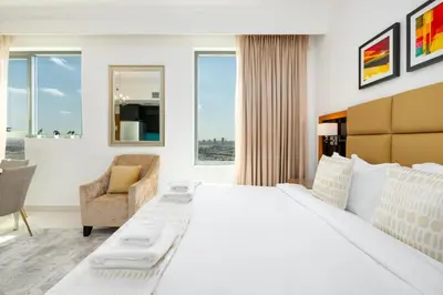 a white bedroom with a large bed and a chair at Vacay Lettings - DAMAC Capital Bay Tower in Dubai