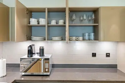 a kitchen with a coffee maker and dishes on shelves at Spacious 1BR with Pool, Gym & Kids Play Area in Dubai