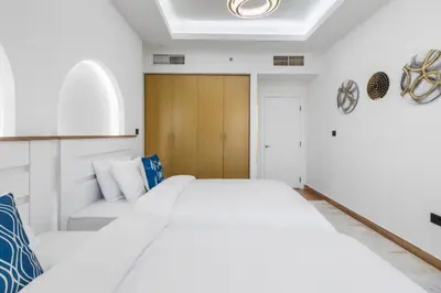 a bedroom with two white beds and a wooden door at 2BR Marina View - Beach Access - Sleeps 8 in JBR in Dubai