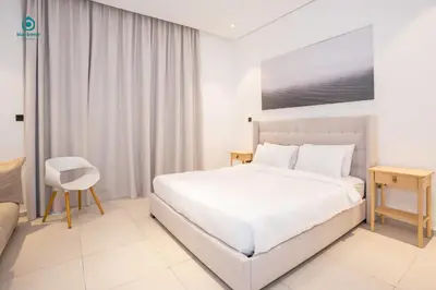 a white bedroom with a bed and a chair at Blue Breeze - Elegant 1BR with Private Jacuzzi & Terrace in JVC in Dubai