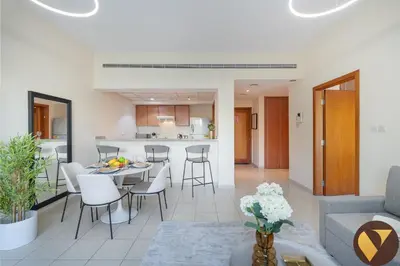 a living room and kitchen with a table and chairs at Vogue The Greens Al Dhafrah near Mall of the Emirates, One Bedroom Apartment with Balcony and vibrant community view, Access to all Amenities in Dubai