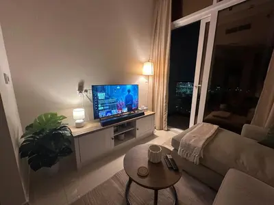 a living room with a couch and a television at Cozy Golf & Lake View 1BR Apartment,Damac Hills 1 in Dubai