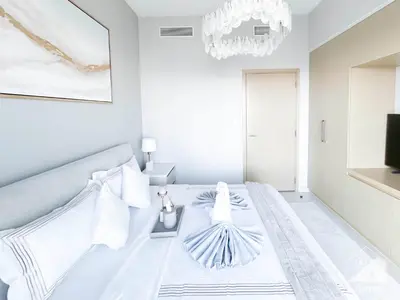 a white bedroom with a bed and a chandelier at Burj Royale Luxury One-Bedroom with City Views in Dubai