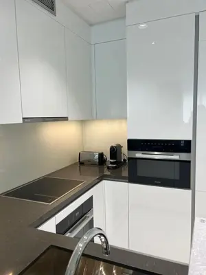 a kitchen with white cabinets and black appliances at 2 Bedrooms - District One Residences 13 in Dubai