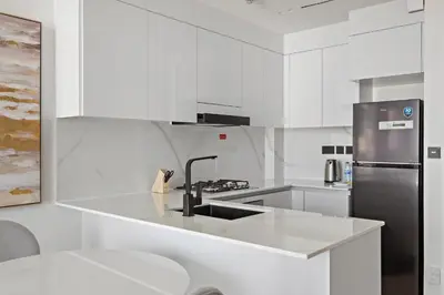a white kitchen with a sink and a refrigerator at Modern and High Floor 1BR at Binghatti Emerald in Dubai