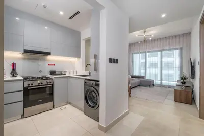 a kitchen with a washer and dryer and a living room at Chic 1 Bed in Creek Side with Terrace in Dubai