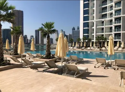 a pool with chairs and umbrellas next to a building at Luxurious studio in Damac maison prive by Phineek vacation home in Dubai