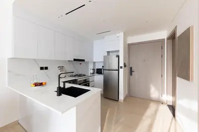 a white kitchen with white counters and a refrigerator at Cozy 1BR with balcony in Binghatti Emerald in Dubai