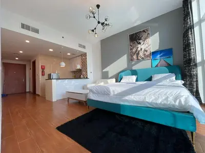 a large bedroom with a blue bed and a kitchen at Studio apartment in jumeriah village triangle district 2 in Dubai