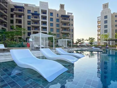 a pool with three white chairs in front of a building at 1 Bedroom Apartment with Burj AlArab View from your Balcony R507 in Dubai