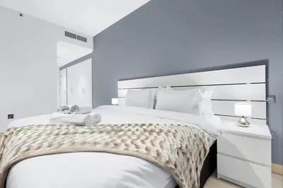 a white bedroom with a large bed with a white headboard at Luxury 2BR Apartment Near JBR Beach with Pool and Gym Access in Dubai
