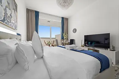 a white bedroom with a large bed and a television at Stylish Studio Close To Metro at Pearlz by Danube in Dubai