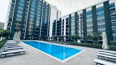 a swimming pool with chairs and umbrellas in front of buildings at One bedroom apartment brand new Dubai Hills ultra luxury furniture in Dubai