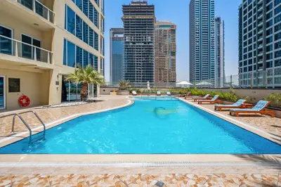 a large swimming pool with chairs and buildings at Modern Studio Apartment in Lake View in Dubai