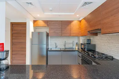 a kitchen with wooden cabinets and a stainless steel refrigerator at Escape24 Modern 1BR with Pool View in JVC in Dubai