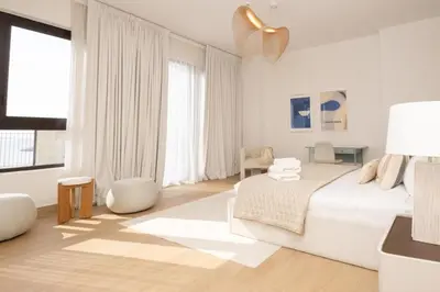 a white bedroom with a bed and a large window at HiGuests - Experience Coastal Elegance at La Rive 2 in La Mer in Dubai