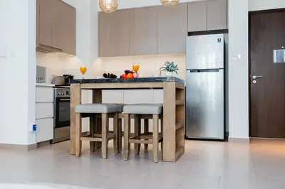 a kitchen with a counter with stools and a refrigerator at Comfortable Stylish Haven - Great Community in Dubai