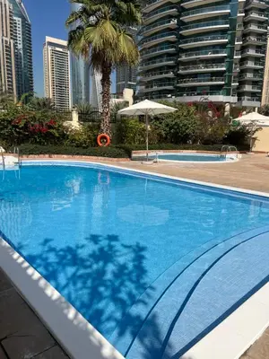 a large blue swimming pool with a palm tree and buildings at One bed apartment at a great location in Dubai Marina in Dubai