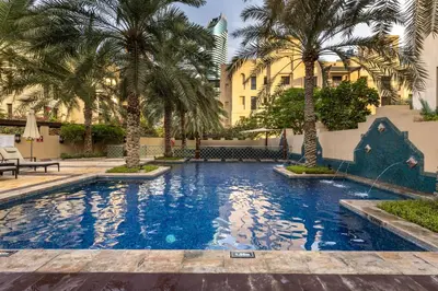a swimming pool with palm trees and a building at Maison Privee - Stylish & Spacious Apartment in Downtown Dubai in Dubai
