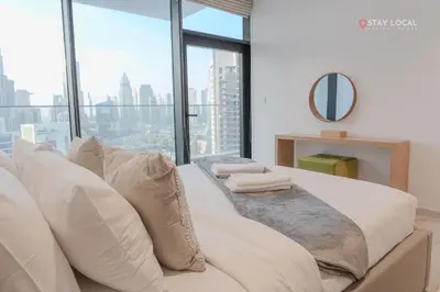 a bedroom with a large white bed with a large window at Experience Iconic Burj Khalifa Views from Your Cozy Getaway with Pool in Dubai