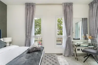 a bedroom with a bed and a desk and windows at White Sage Brand New 3BR Villa with Garden and Two Balconies in Dubai