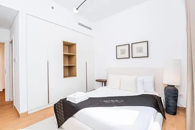 a white bedroom with a bed and a lamp at Escape24 Luxury 2BR Sea View with Beach Access in La Mer in Dubai