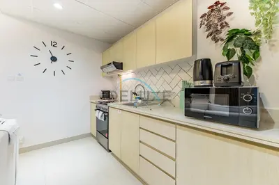 a kitchen with a microwave and a clock on the wall at Charming 1BR in Dania 3, IMPZ by Deluxe Holiday Homes in Dubai