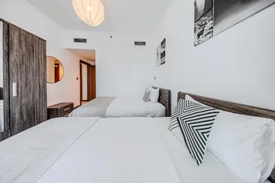 a white bedroom with two beds and a chandelier at 2BR apartment in Missoni in Dubai