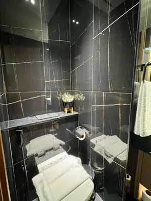 a black tiled bathroom with a toilet and a mirror at Modern & Elegant 1br Apartment In Jvc in Dubai