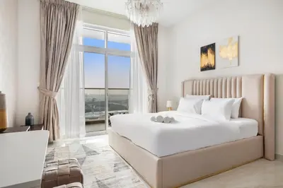 a white bedroom with a large bed and a window at Lux Studio Apt near Butterfly Garden - Pool & Gym in Dubai