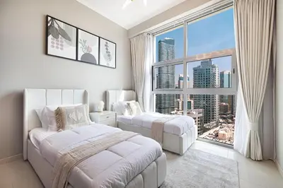 a white bedroom with two beds and a large window at Cozy Urban 2BR Apartment in DEC Tower Marina in Dubai