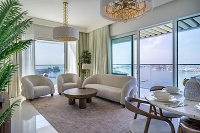 a living room with a table and chairs and windows at Homes Beyond l Elegant 2BR with Wide Sea Views in Dubai