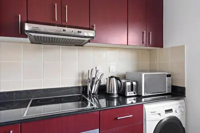 a kitchen with red cabinets and a stove and a microwave at Time Place Near Metro and Mall in Dubai
