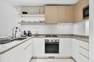 a white kitchen with white cabinets and appliances at Stylish 1BR APT with Gym, Pool & Private Parking in Dubai