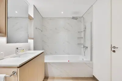 a white bathroom with a shower and a sink at Stylish 1BR APT with Gym, Pool & Private Parking in Dubai
