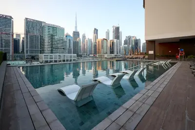 a swimming pool with white chairs and a city skyline at Full Burj Khalifa & Canal View I 7 Mins to Dubai Mall I Exclusive 2BHK For Up to 6 People in Dubai