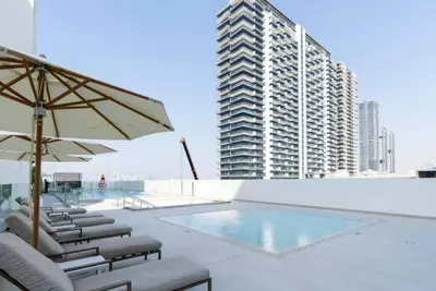 a pool with chairs and an umbrella and a building at Bright 1br Jvc Balcony & Free Parking in Dubai